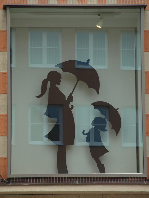 Illustrated window decal of a woman and child holding umbrellas in silhouette against a building facade with reflected windows